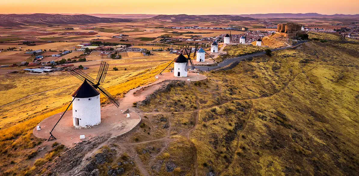 Ayudas+Rural Vista aérea de los molinos de viento de Consuegra, un símbolo de la cultura española. La imagen representa la esencia del medio rural, reflejando el impulso de proyectos sociales como el programa Ayudas+Rural 2025 para mejorar la vida en estas zonas con 18 millones de euros.