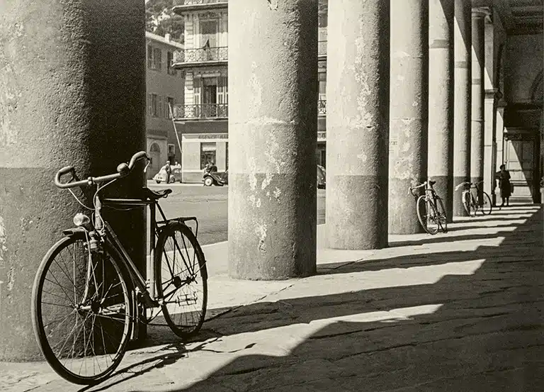 Joaquín Tusquets de Cabirol Bicicleta aparcada junto a una columna de piedra bajo una galería porticada.