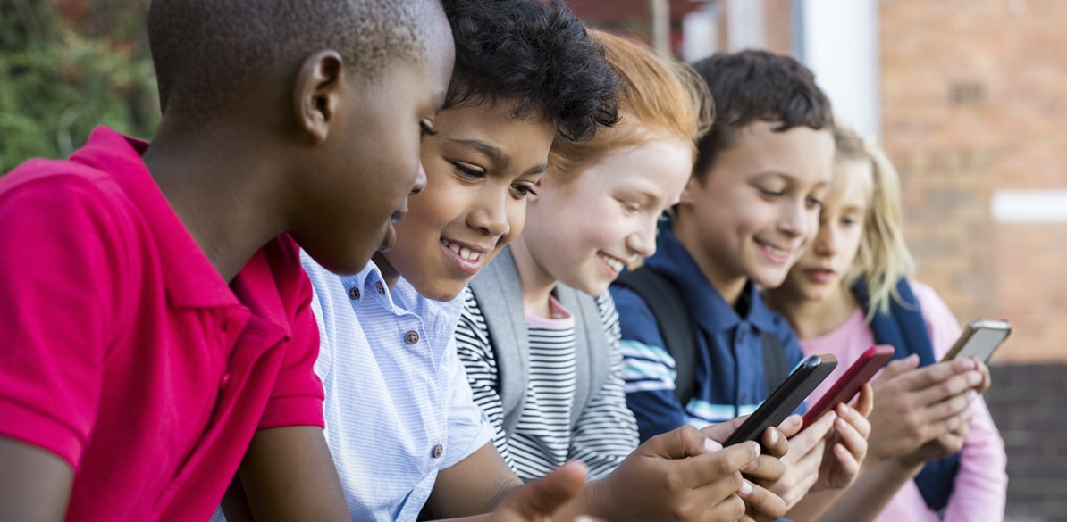 Grupo de cinco niños de diversas etnias concentrados en sus dispositivos móviles mientras exploran tecnologías de la información y comunicación