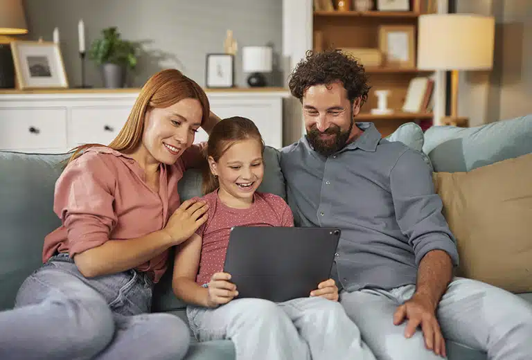 Guías Familia con una niña utilizando una tablet en el sofá de casa mientras comparten un momento juntos.